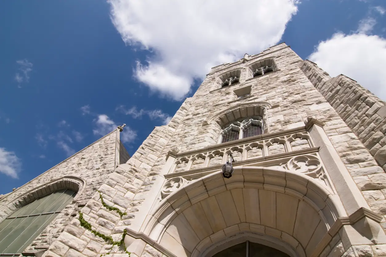 Stone church tower under a bright blue sky with clouds.